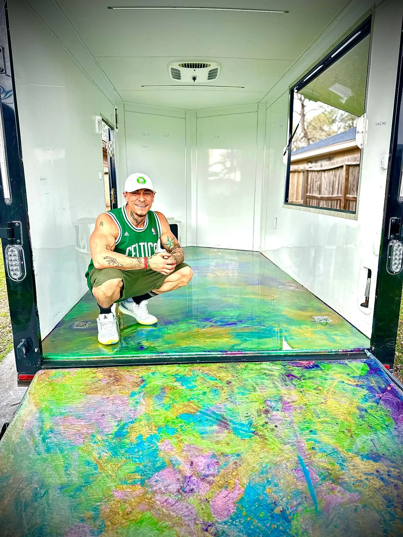 Blake Mendoza crouching beside a vivid green, turquoise, gold, and purple epoxy floor inside an enclosed trailer
