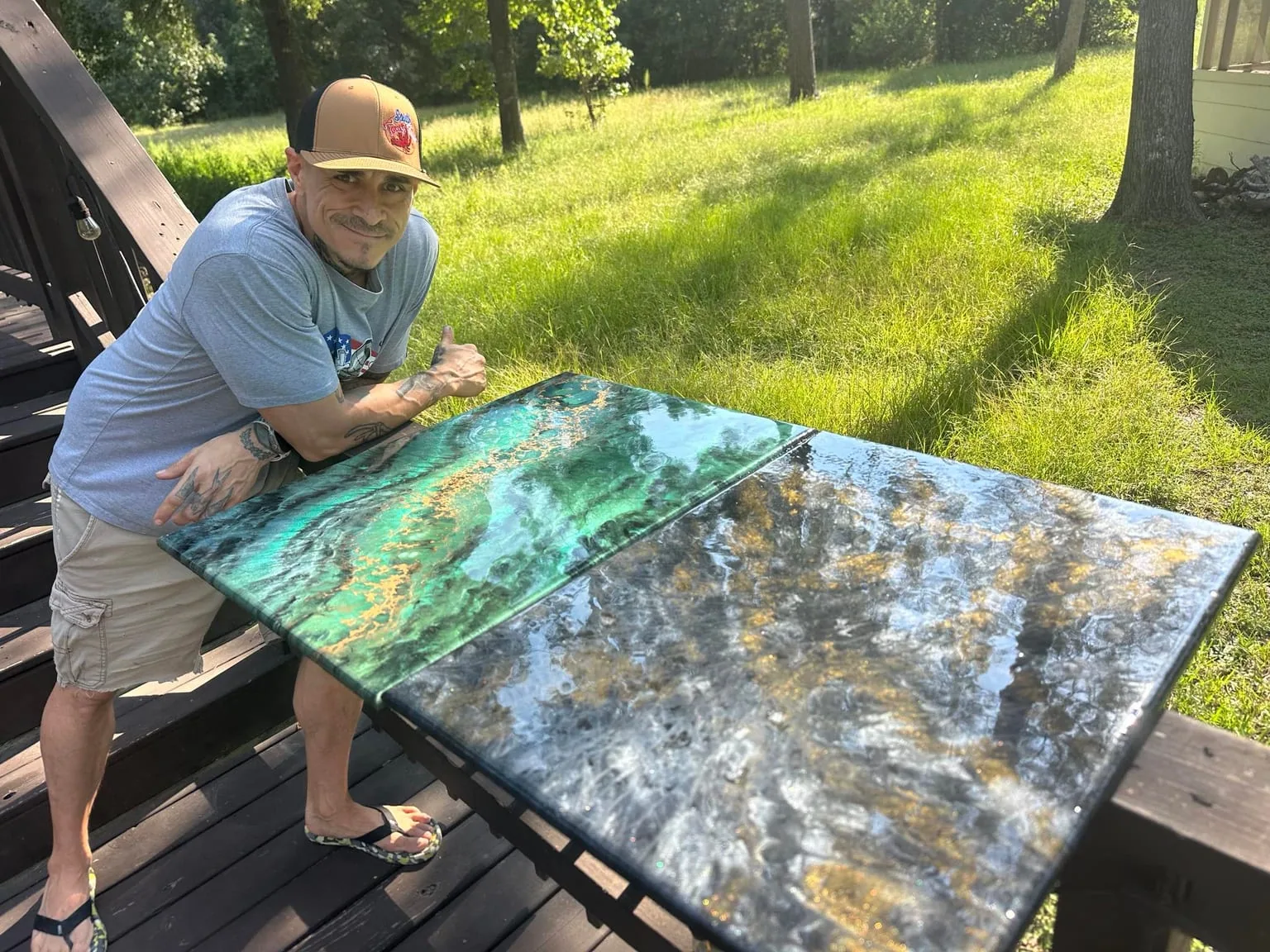 Blake Mendoza beside glossy green, black, and gold custom resin tables on an outdoor deck
