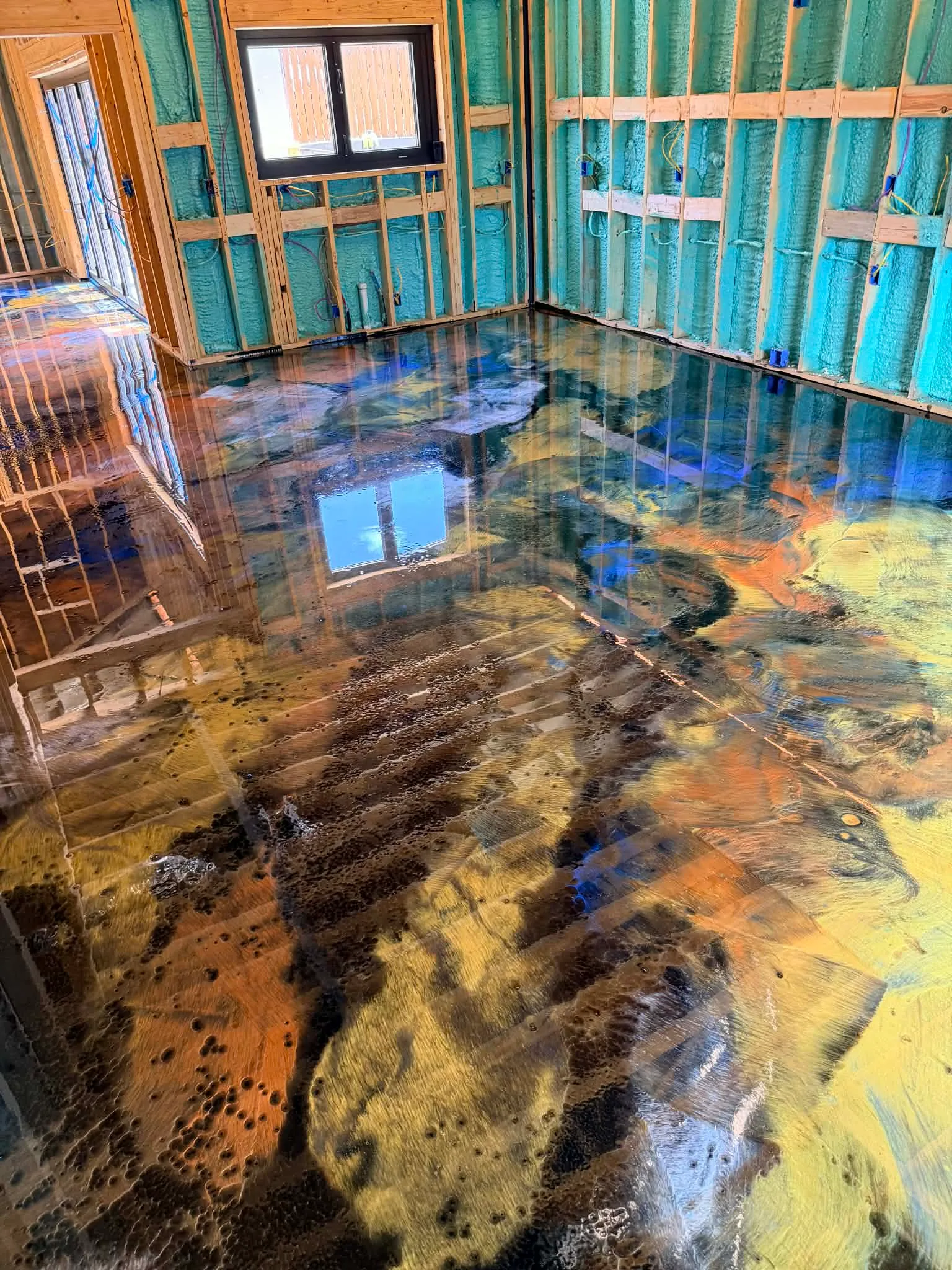 Metallic epoxy floor reflecting a window beside blue wall insulation and exposed framing